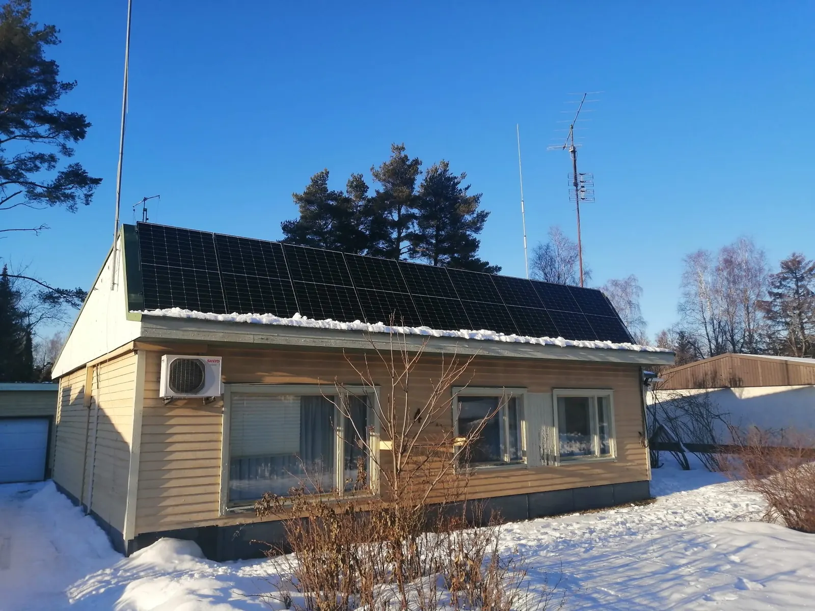 Solar panels on the roof of a light-coloured detached house in a snowy yard