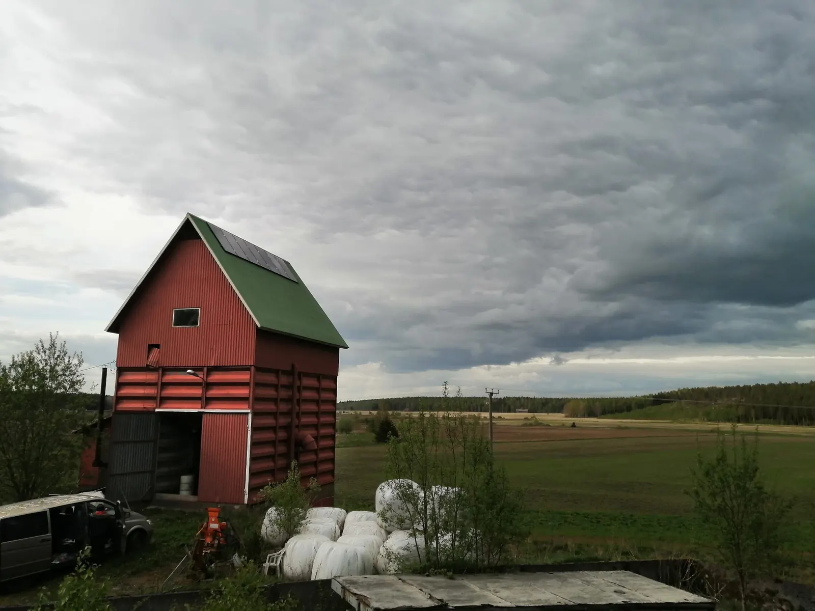 Solar panels on the roof of a red farm building at the edge of open fields