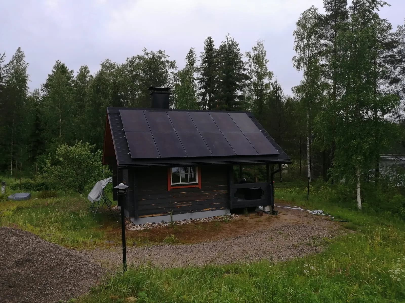 Solar panels on the roof of a dark log cabin surrounded by forest