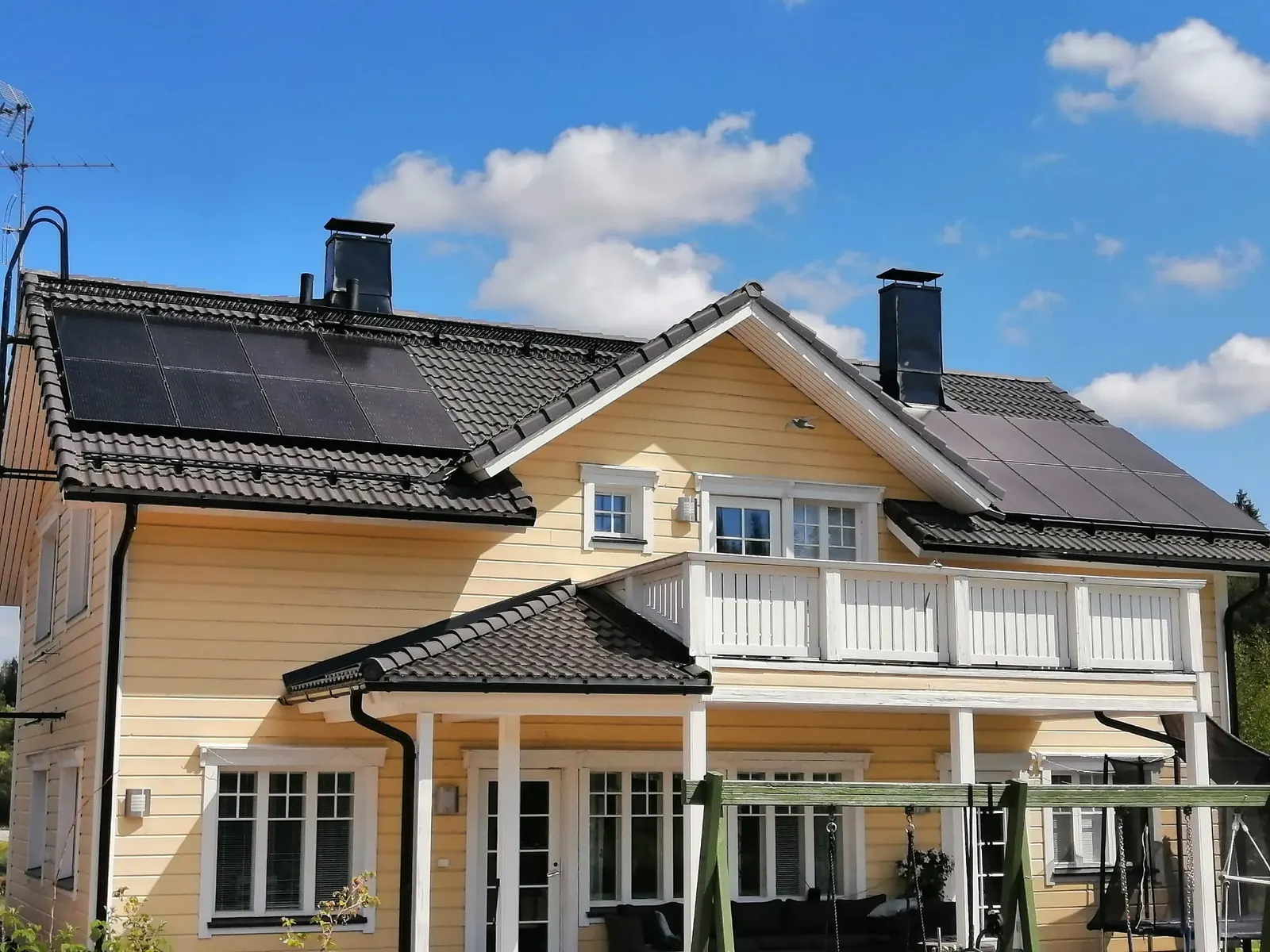 Solar panels on the tiled roof of a yellow two-storey wooden house